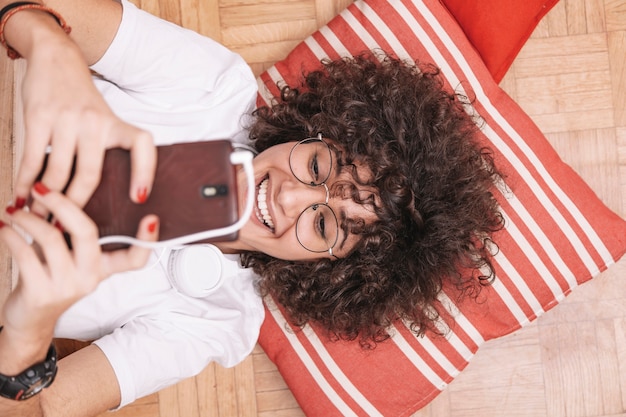 Desde arriba adolescente sonriendo y usando teléfono inteligente