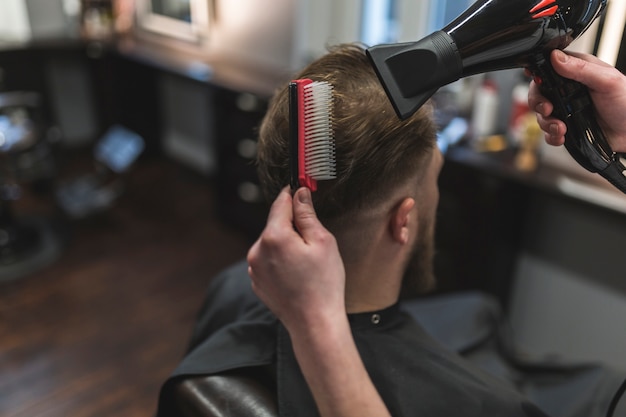 Desde arriba barbero peinando y secando el cabello del cliente