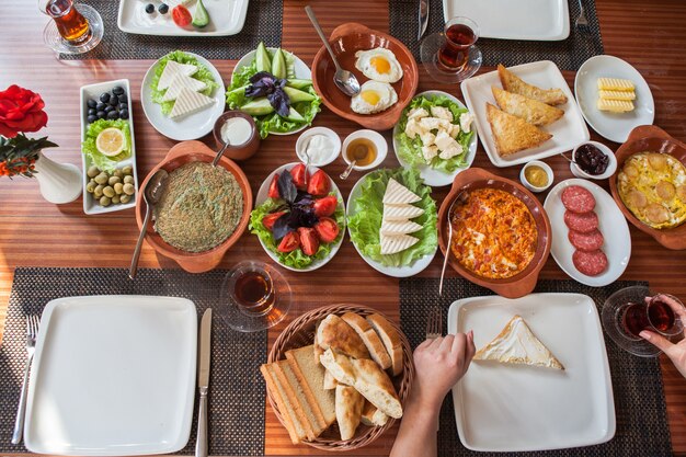 Desde arriba desayuno variado con tortilla y vaso de té y mano humana en servilletas