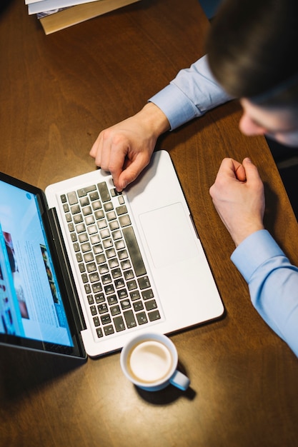 Desde arriba, el hombre busca una computadora portátil cerca de una taza de café