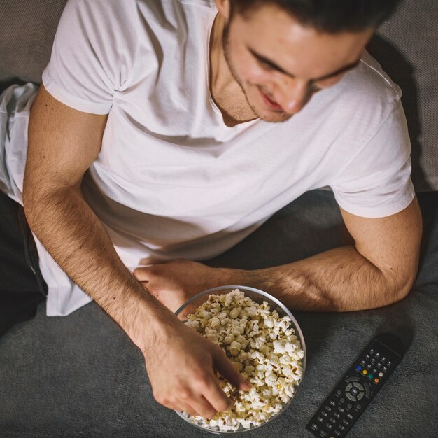 Desde arriba, hombre comiendo palomitas de maíz en el sofá