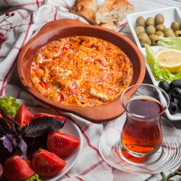 Desde arriba huevos fritos con tomates con un vaso de té y tomates y aceitunas variadas en plato de arcilla