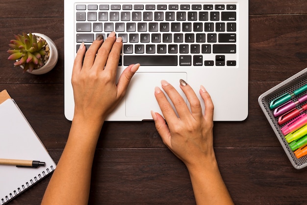 Desde arriba de manos femeninas trabajando en laptop.