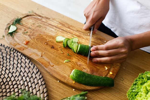 Desde arriba, la mujer está cortando un pepino en el escritorio de la cocina.