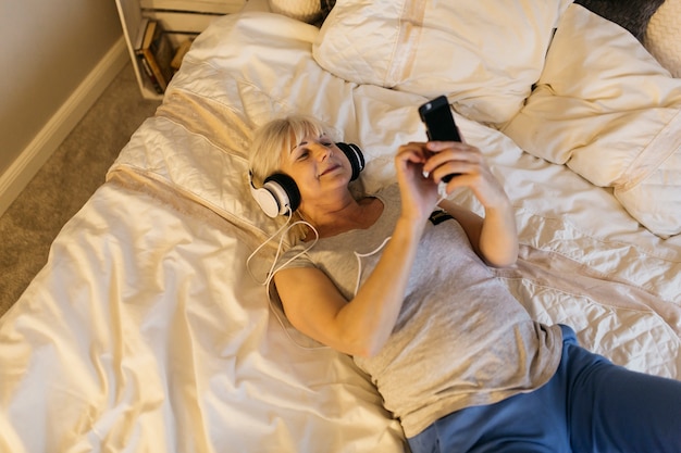 Desde arriba mujer mayor escuchando música en la cama