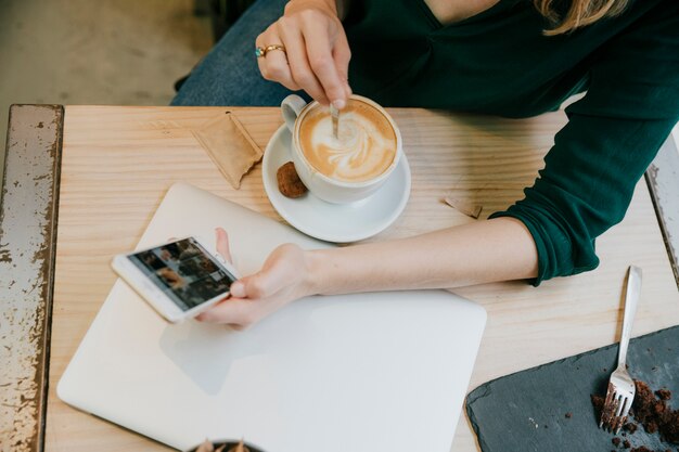 Desde arriba, mujer mezclando café y usando un teléfono inteligente