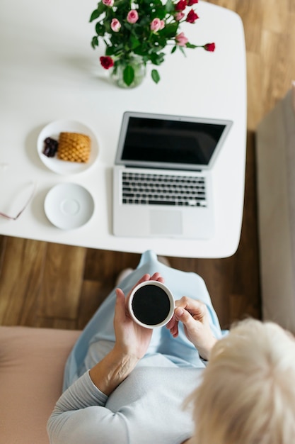 Foto gratuita de arriba mujer tomando café cerca de la computadora portátil