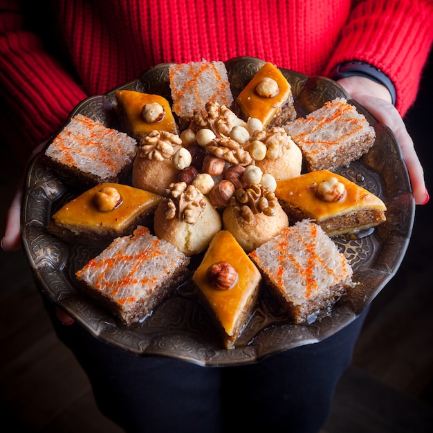 Foto gratuita desde arriba surtido al horno con baklava y baklava sheki y mano humana en placa de cobre