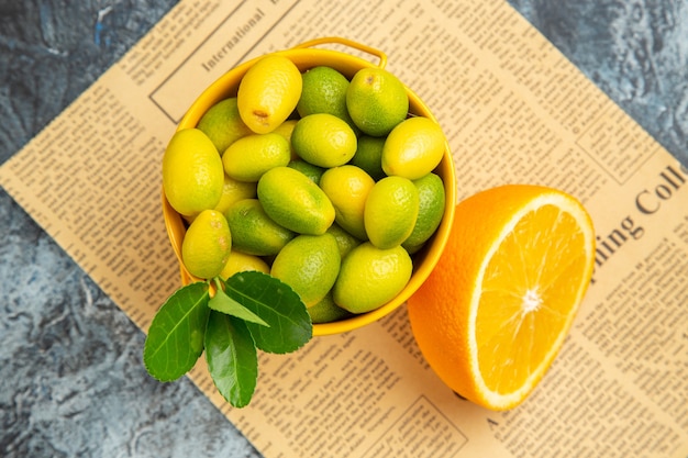 Arriba vista cercana de frutas cítricas en una canasta de periódico sobre fondo gris