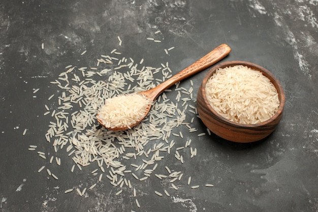 arroz arroz en el cuenco de madera y cuchara sobre la mesa oscura