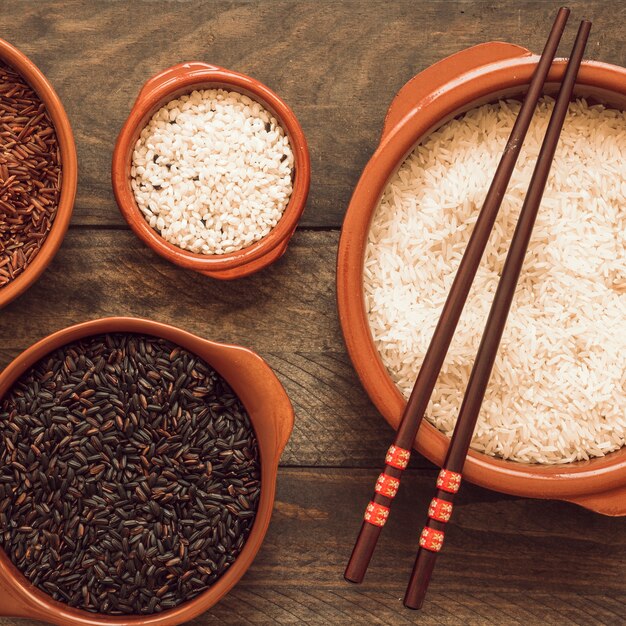 Arroz blanco crudo; cuencos de arroz rojo arroz negro y jazmín en la mesa de madera