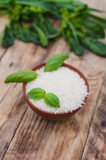 Arroz blanco crudo en un tazón con hojas frescas de albahaca sobre un tablón de madera desgastado