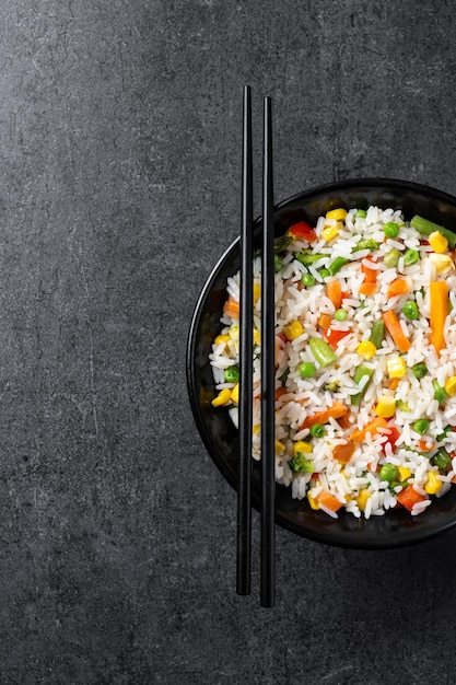 Arroz blanco con verduras en un cuenco negro sobre un fondo negro