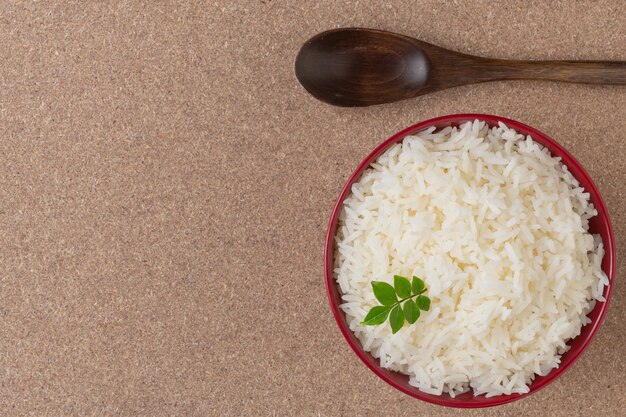 Arroz cocido en una taza roja colocada en el piso de madera contrachapada.