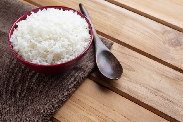 Arroz cocido en una taza roja colocada en el piso de madera contrachapada.