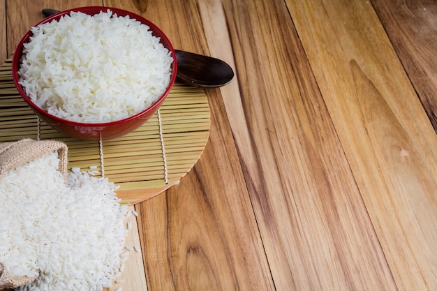 Arroz cocido en una taza roja colocada en el piso de madera contrachapada.