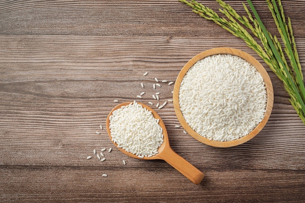 Arroz en cuenco de madera y cuchara de madera con planta de arroz