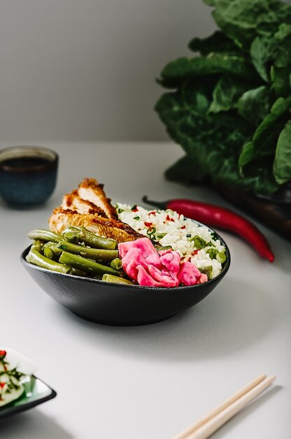 Arroz con especias, salsa de soja y gajos de pavo en un cuenco negro con judías verdes salteadas, pimientos picantes, chucrut y daikon. De cerca, enfoque selectivo con espacio de copia. Idea de comida asiática