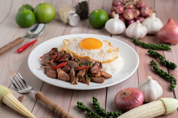 Arroz frito con albahaca santa con corazón de pollo y huevo frito sobre un piso de madera blanca.