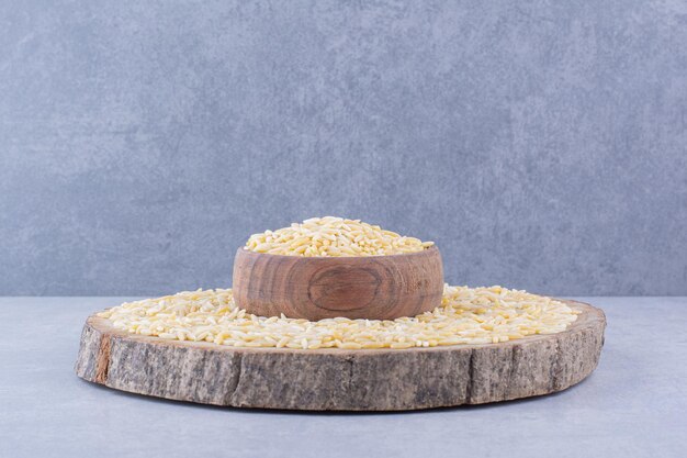 Arroz integral apilado sobre una rodaja de tronco con un tazón lleno en el medio, sobre una superficie de mármol