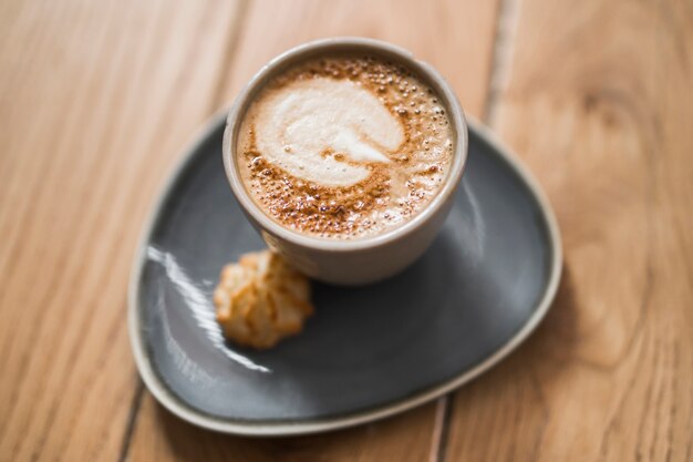 El arte del capuchino en una taza de cerámica con galleta sobre la mesa de madera