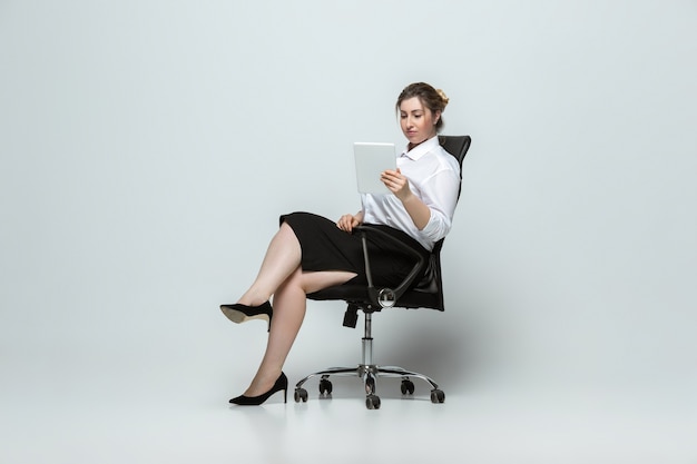 Foto gratuita artilugio. mujer joven en traje de oficina. carácter femenino positivo del cuerpo, feminismo, amarse a sí misma, concepto de belleza. plus size empresaria en pared gris. jefe, hermoso. inclusión, diversidad.