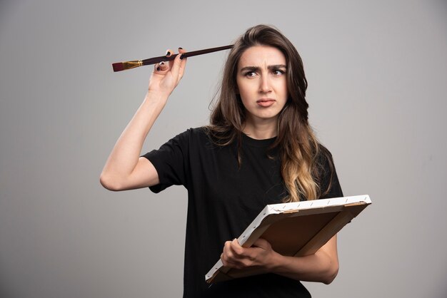 Artista femenina en camisa negra tocando su cabeza con un cepillo.