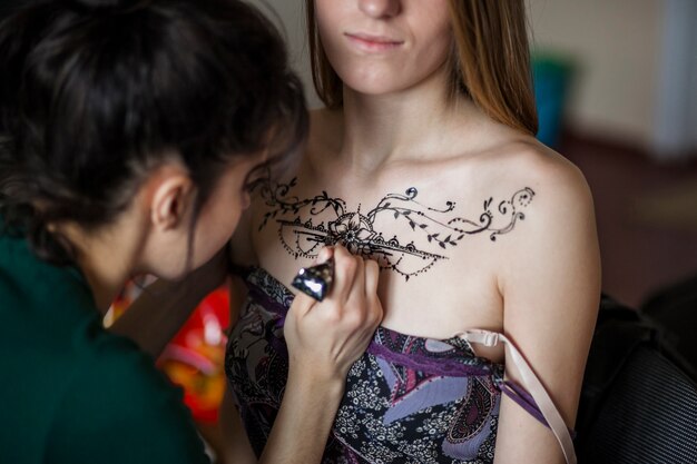 Artista femenina dibujando el tatuaje de mehndi en el pecho de la mujer.