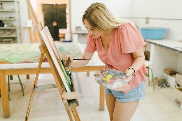 Artista femenina haciendo pintura sobre caballete con pincel