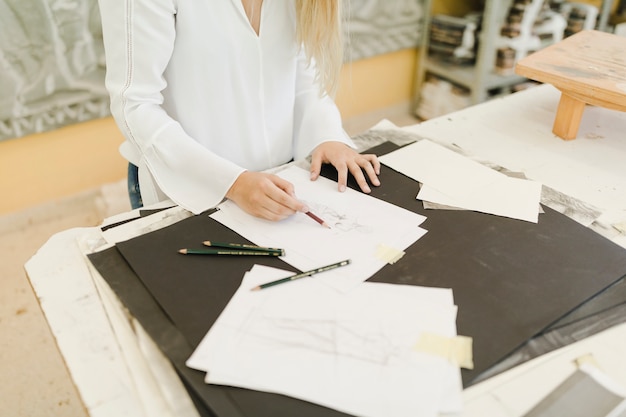 Artista femenina que bosqueja en el papel con el lápiz en la tabla