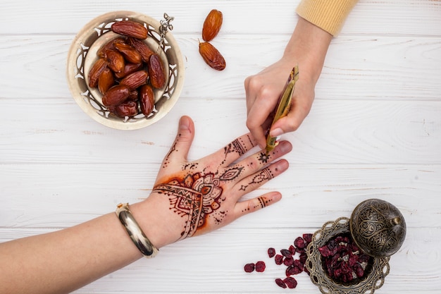 Foto gratuita artista haciendo mehndi en mano de mujer cerca de fechas fruta