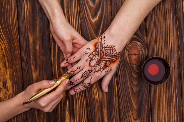 Artista haciendo mehndi en mano de mujer cerca de taza de té