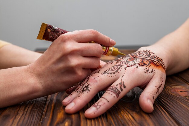 Artista haciendo mehndi en mano de mujer en mesa