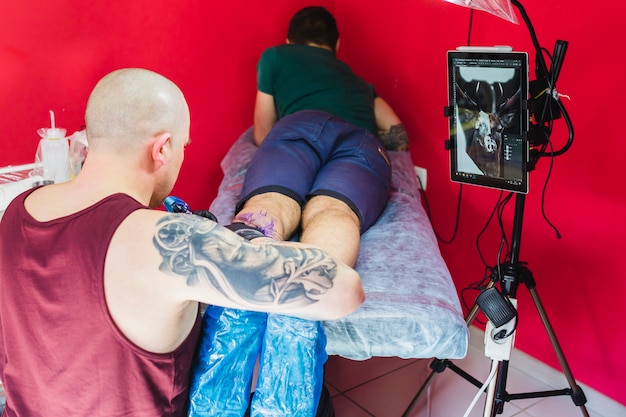 Artista haciendo tatuaje en la pierna en el taller