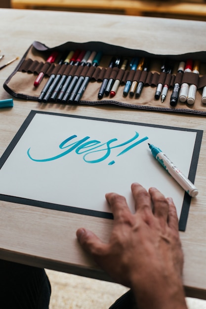 Artista ilustrador joven inconformista en camiseta negra simple crea un dibujo de letras a mano auténtico y único en su brillante estudio industrial