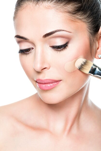 Artista de maquillaje aplicando base tonal líquida en el rostro de la mujer