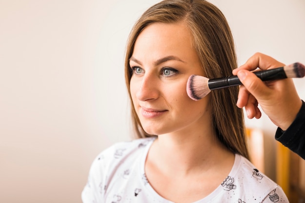 Artista de maquillaje aplicando colorete en la cara de mujer