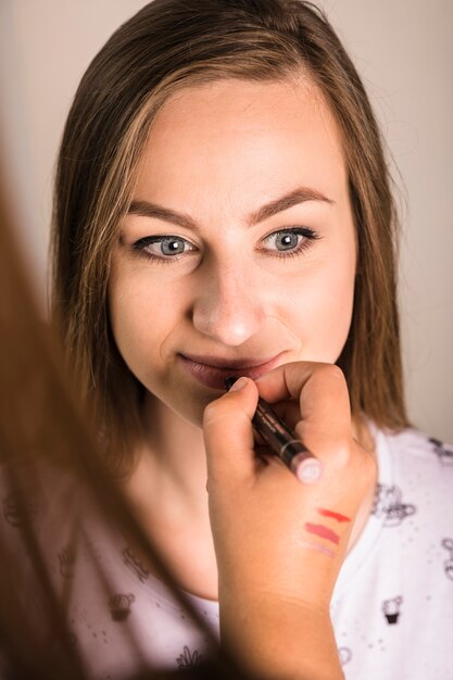Artista de maquillaje aplicando lápiz labial labios de mujer joven atractiva