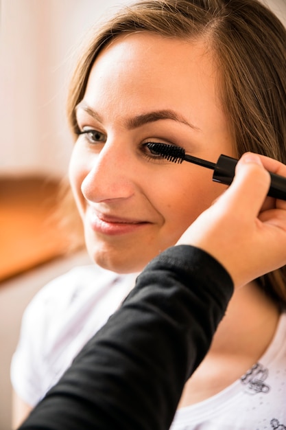 Foto gratuita artista de maquillaje aplicando rimel en la cara de mujer feliz