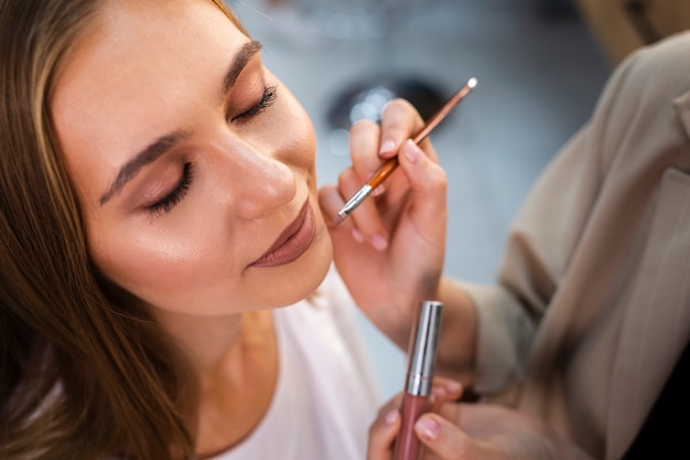 Artista de maquillaje de cerca aplicando lápiz labial desnudo en mujer con pincel