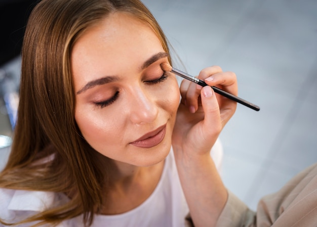 Artista de maquillaje de cerca aplicando sombra de ojos desnuda a mujer con pincel