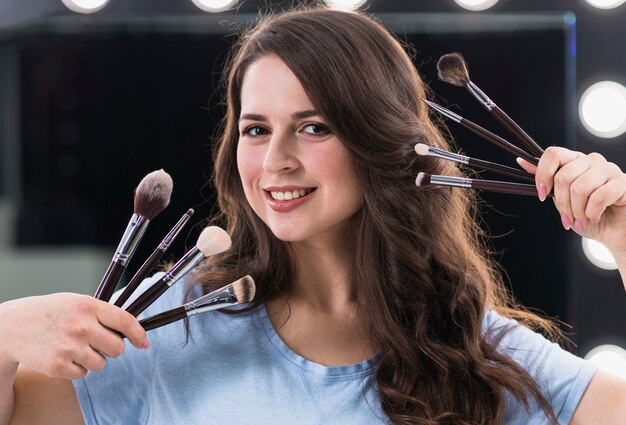 Artista de maquillaje feliz de la mujer con los cepillos