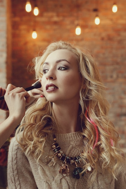 Artista de maquillaje con hermosa mujer rubia