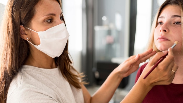 Foto gratuita artista de maquillaje con máscara médica mientras trabaja en el cliente