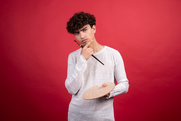 Artista masculino joven posando con paleta y pincel.