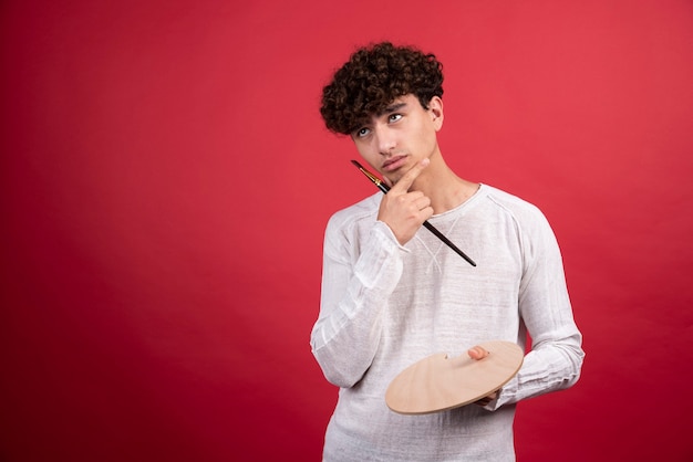 Foto gratuita artista masculino joven posando con paleta y pincel.