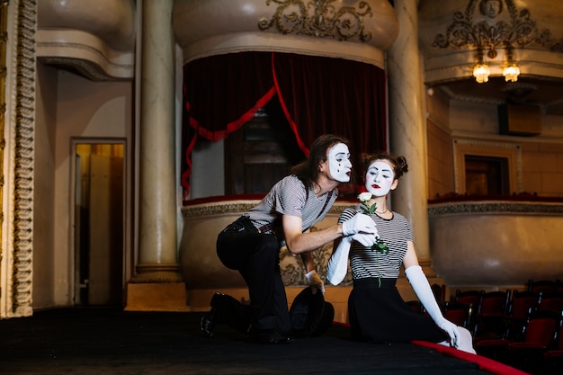 Artista masculino del mime que da la rosa blanca al mime femenino que se sienta en etapa