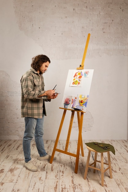 Artista masculino pintando en estudio con acuarelas.