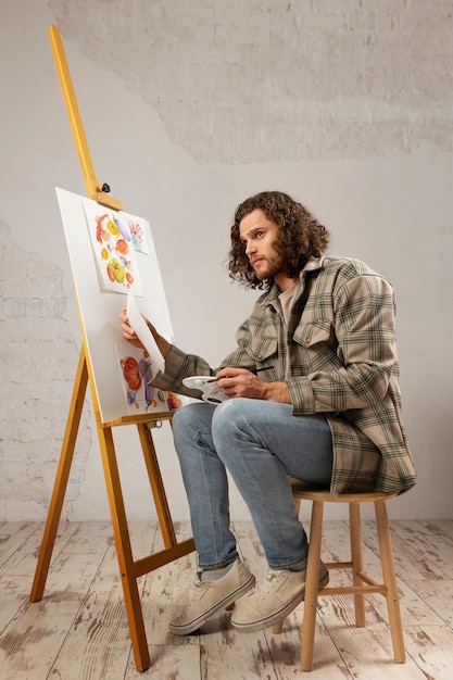 Artista masculino pintando en estudio con acuarelas.