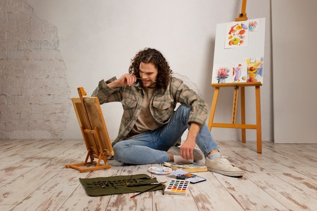 Artista masculino pintando en estudio con acuarelas.